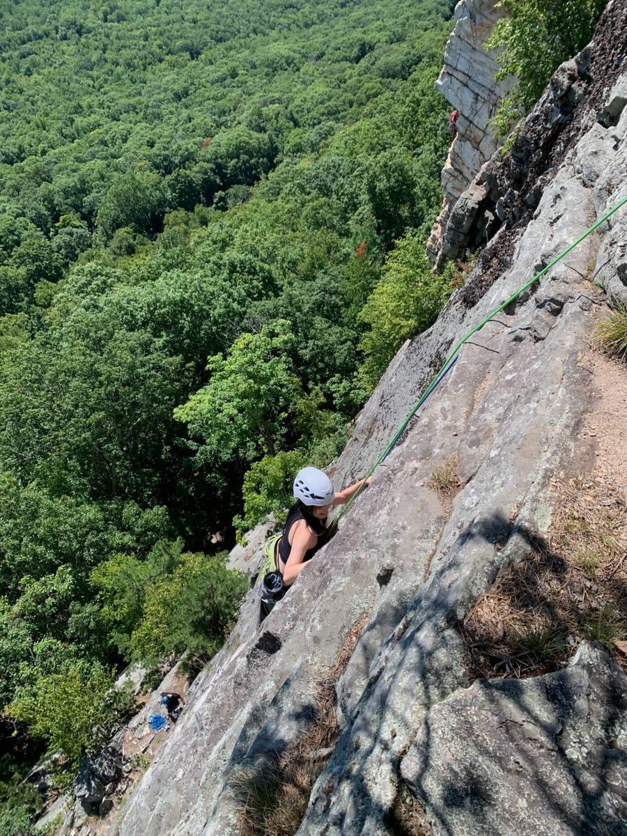 Mengqi climbing a rock face above a forest