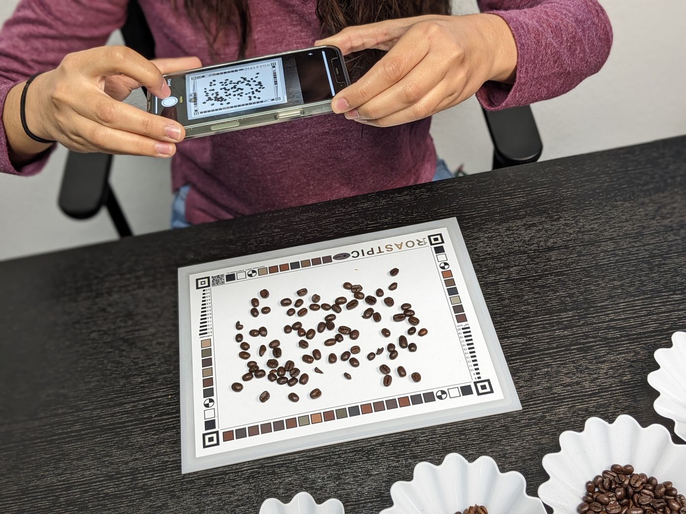 Someone photographing roasted beans laid out on the RoastPic reference sheet.